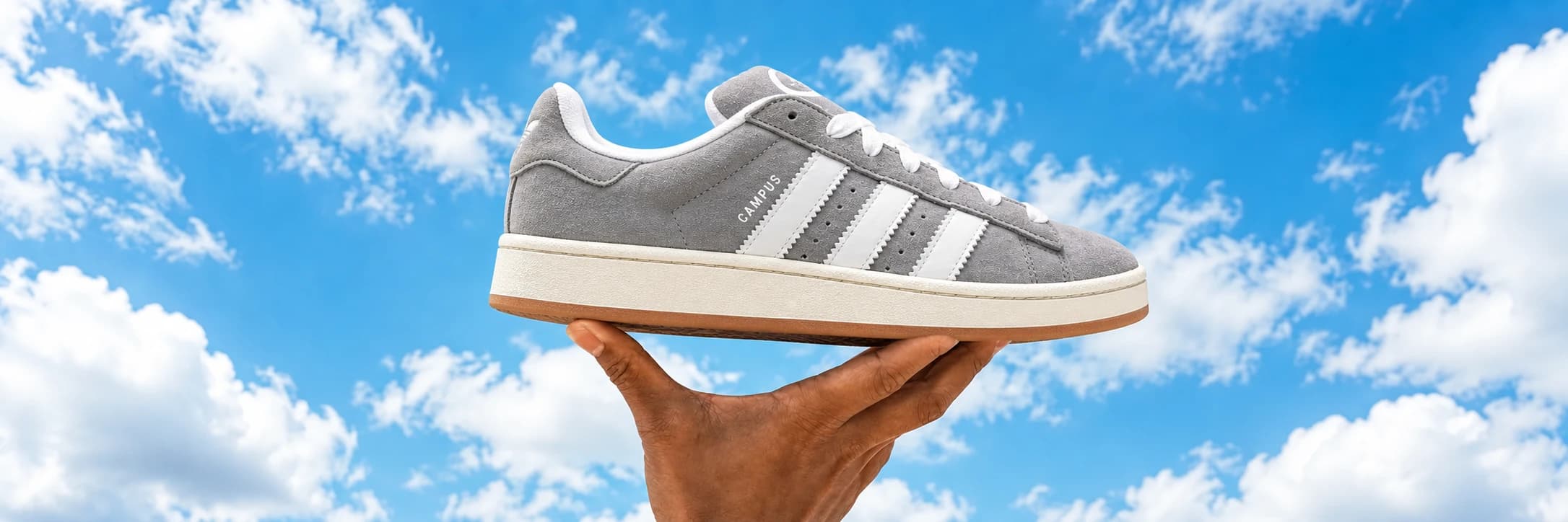 Šedá Adidas Campus 00s s bílými pruhy na ruce proti modré obloze