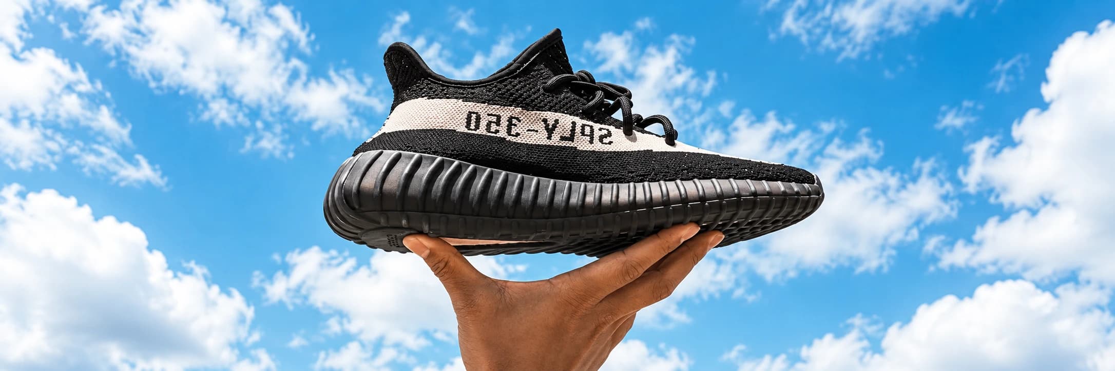 Černá teniska Adidas na ruce proti modré obloze