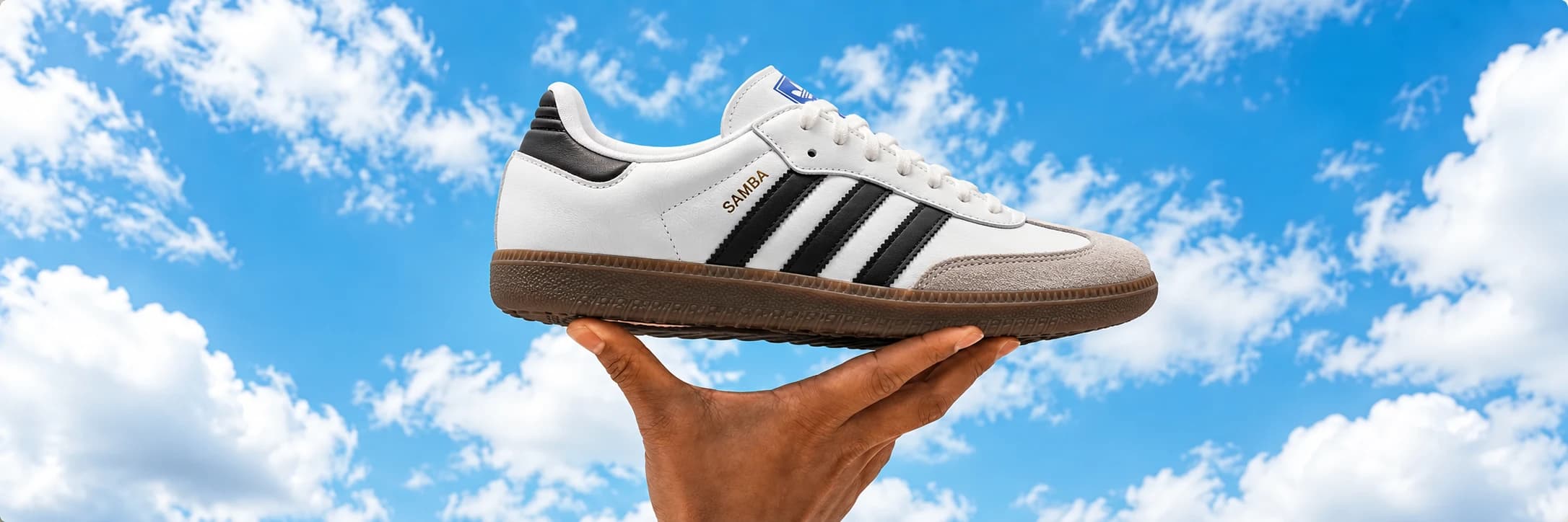 Bílo-černá Adidas Samba OG s gumovou podrážkou na ruce proti modré obloze